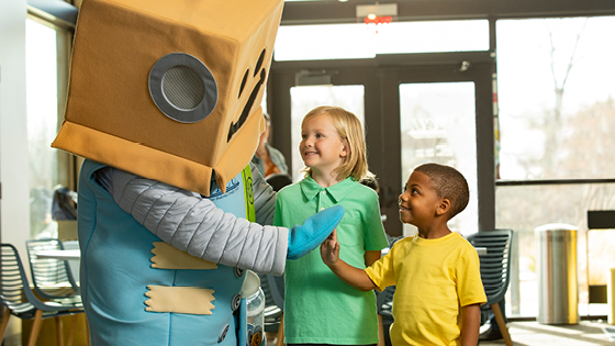 Save-A-Tron standing with two kids and one of them high-fives the mascot