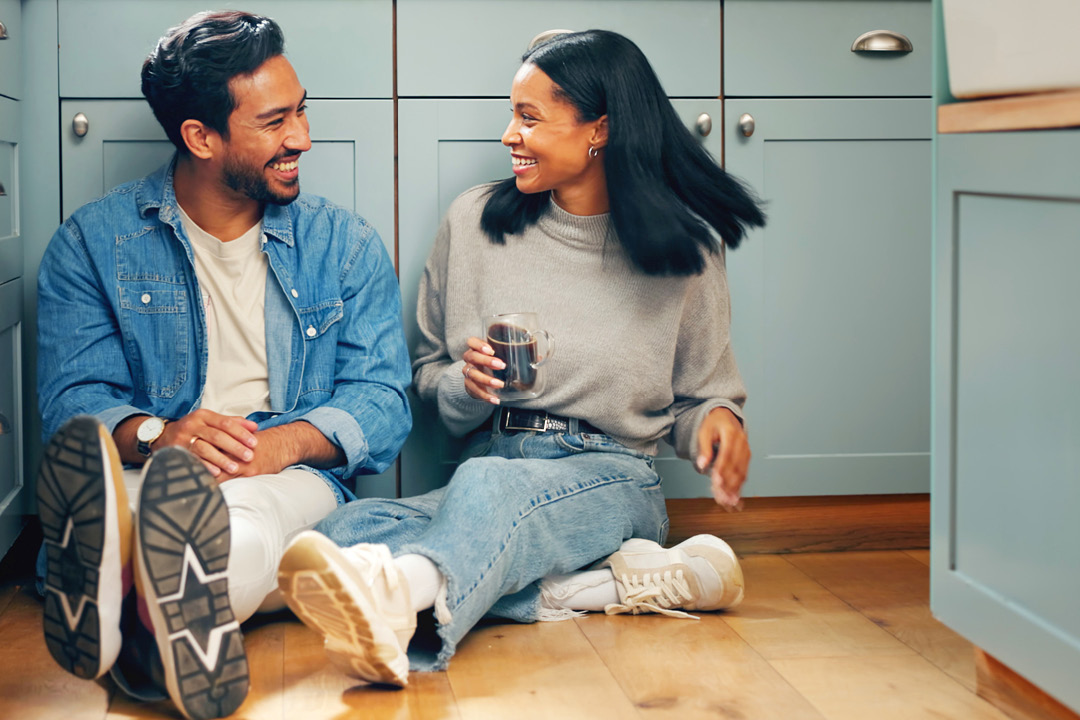 Young man and woman sitting on the floor of their new kitchen.