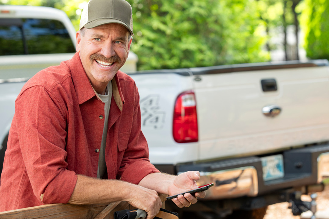 A smiling older man sitting in front of a white truck.