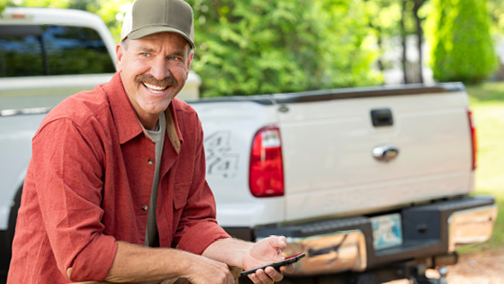 A smiling older man sitting in front of a white truck.