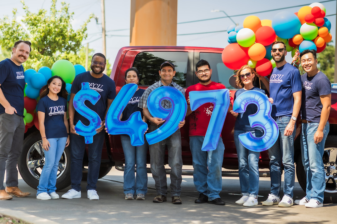 A group of people holding number signs in front of a car and balloons.