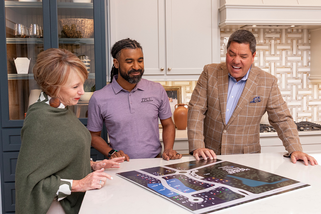Two men and a woman look at a home development map on a kitchen counter