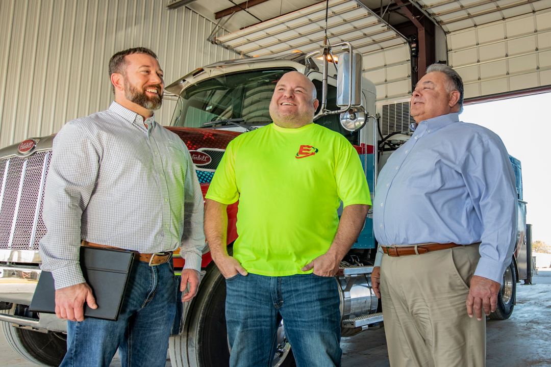 A business owner and two businessmen stand in front of a tractor trailer truck