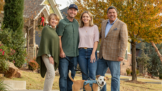 A family consisting of two parents, two adult children and dog stand in a front yard