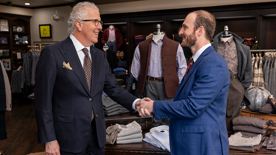 Two men in suites shake hands in a men's clothing store