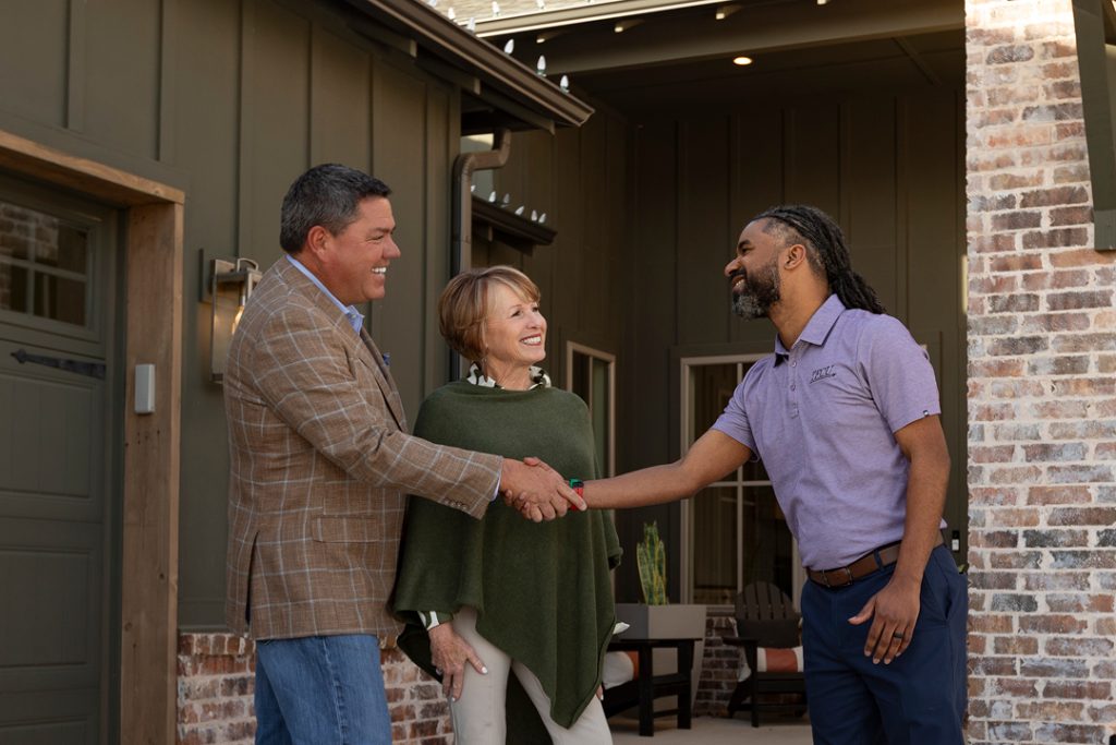 A man smiles and shakes hands with another man and woman