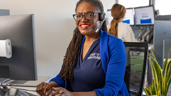 A TFCU employee sits at a desk with a computer wearing a headset.