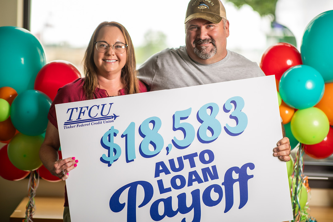 A man and woman hold a sign that says $18,583 Auto Loan Payoff