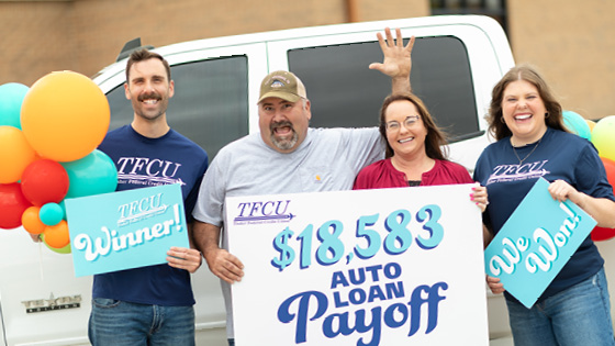 A man and woman hold a sign that says $38,575 Auto Loan Payoff with two TFCU employees
