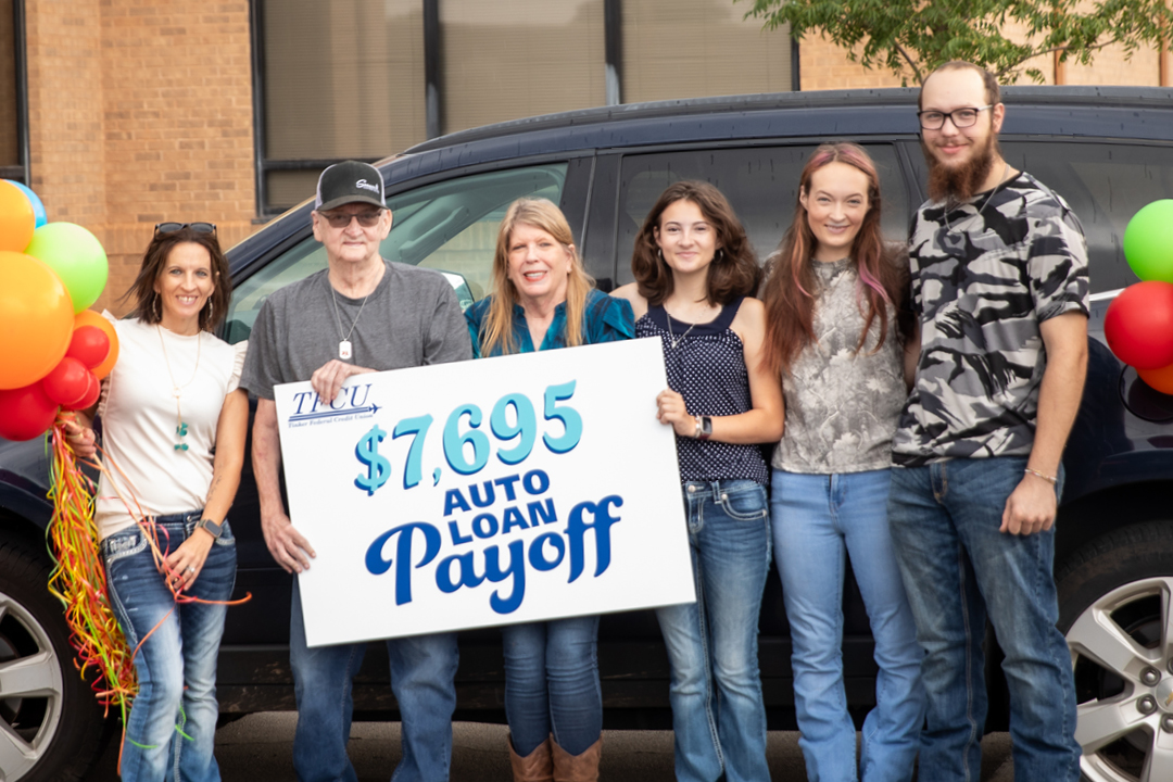 A group of people stand in front of a car holding a sign that says "$7,695 Auto Loan Payoff"