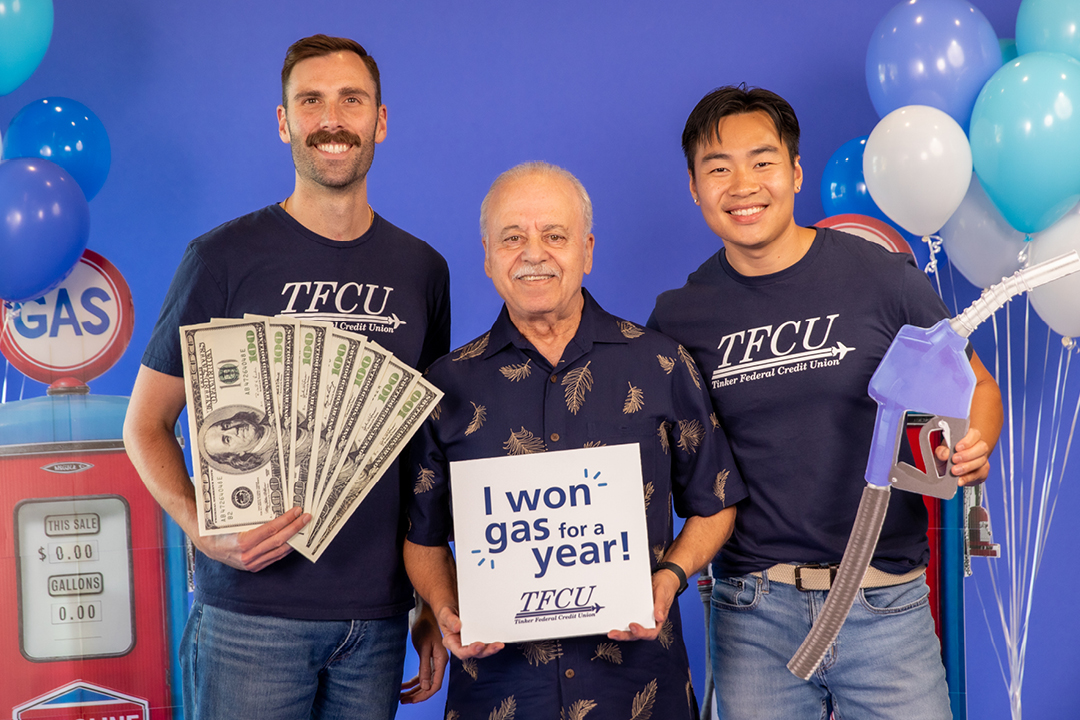 A man stands next to two TFCU employees and holds a sign that says, "I won gas for a year!"