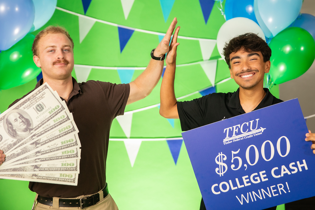 Two college students high five while holding up a sign that reads "$5,000 College Cash winner"