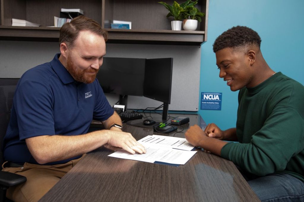 A TFCU employee shows a young man something on a paper while sitting at a desk