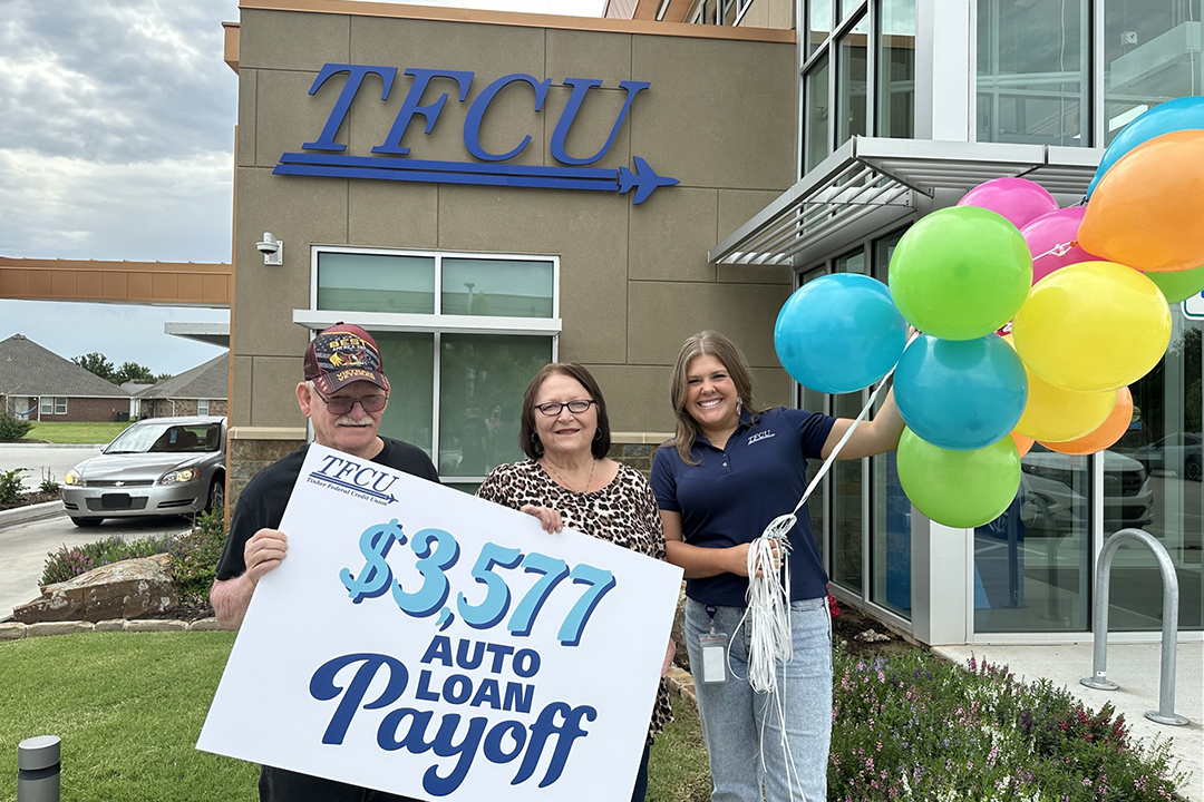 TFCU employee standing with two members holding a sign that says $3,500 auto loan payoff