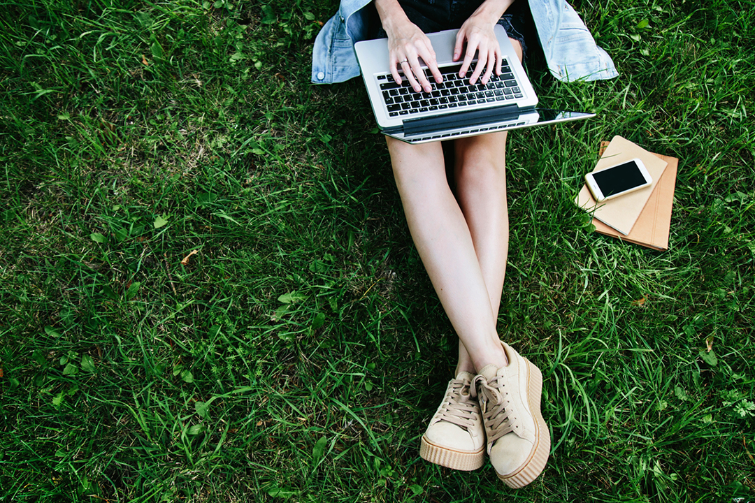 Young girl sitting in grass and typing on her laptop.