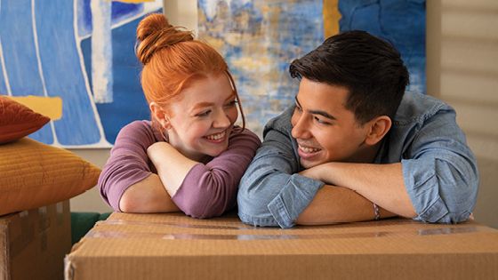 A couple leaning on a box looking at each other.