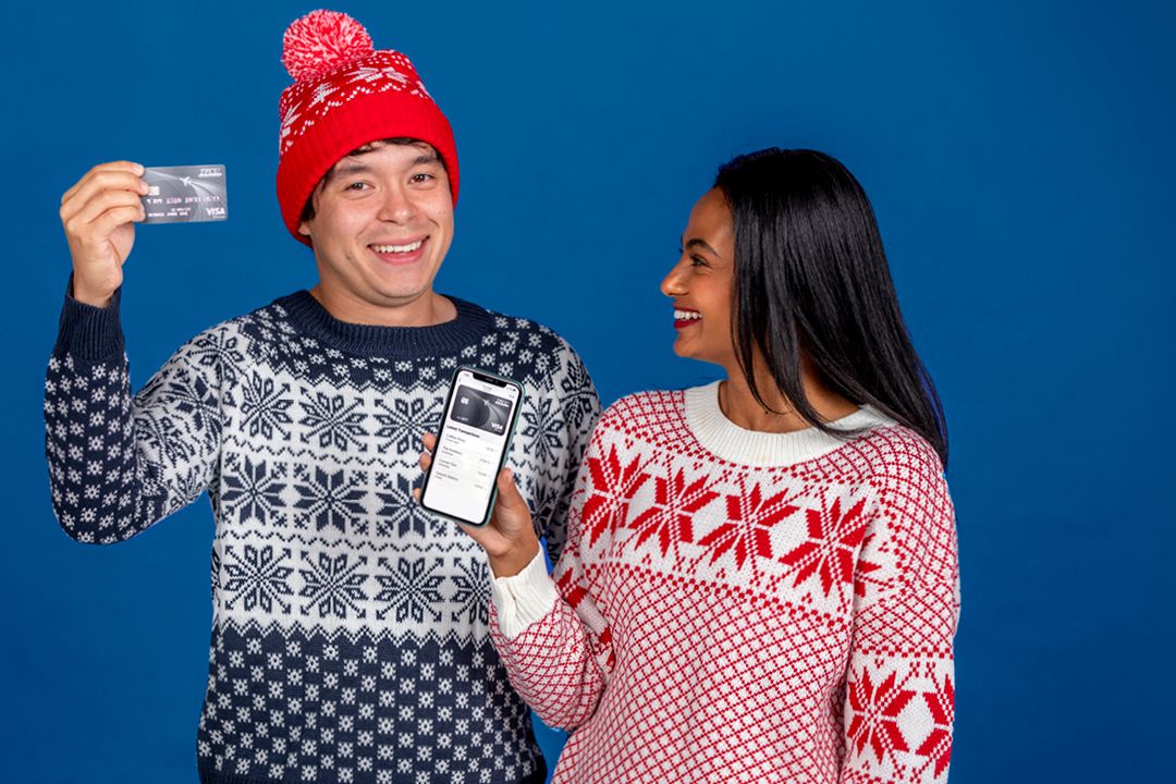 Two people in sweaters and holding a smartphone and credit card