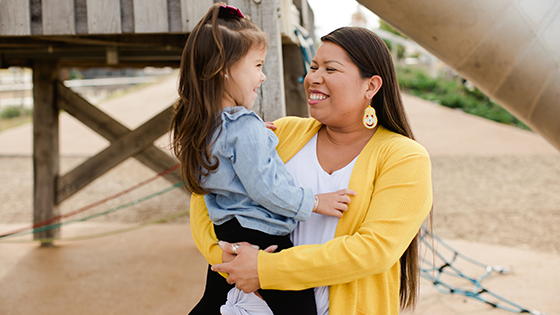 A woman holds a child in front of a playground