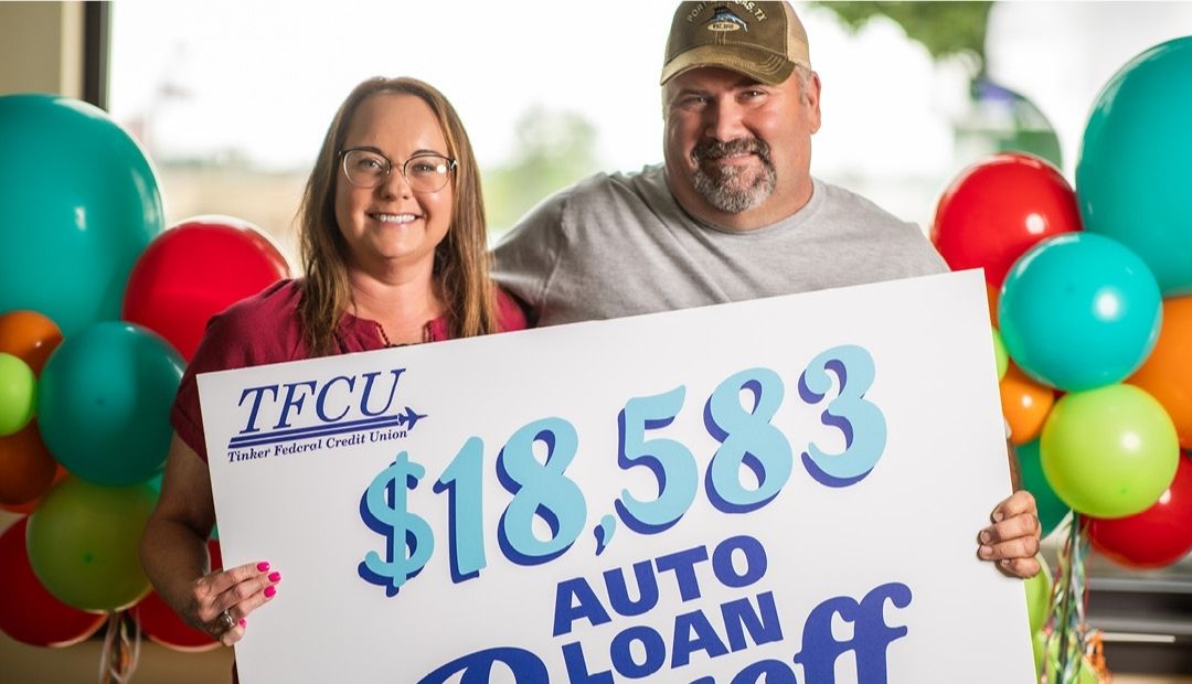 A man and woman hold a sign that says $18,583 Auto Loan Payoff
