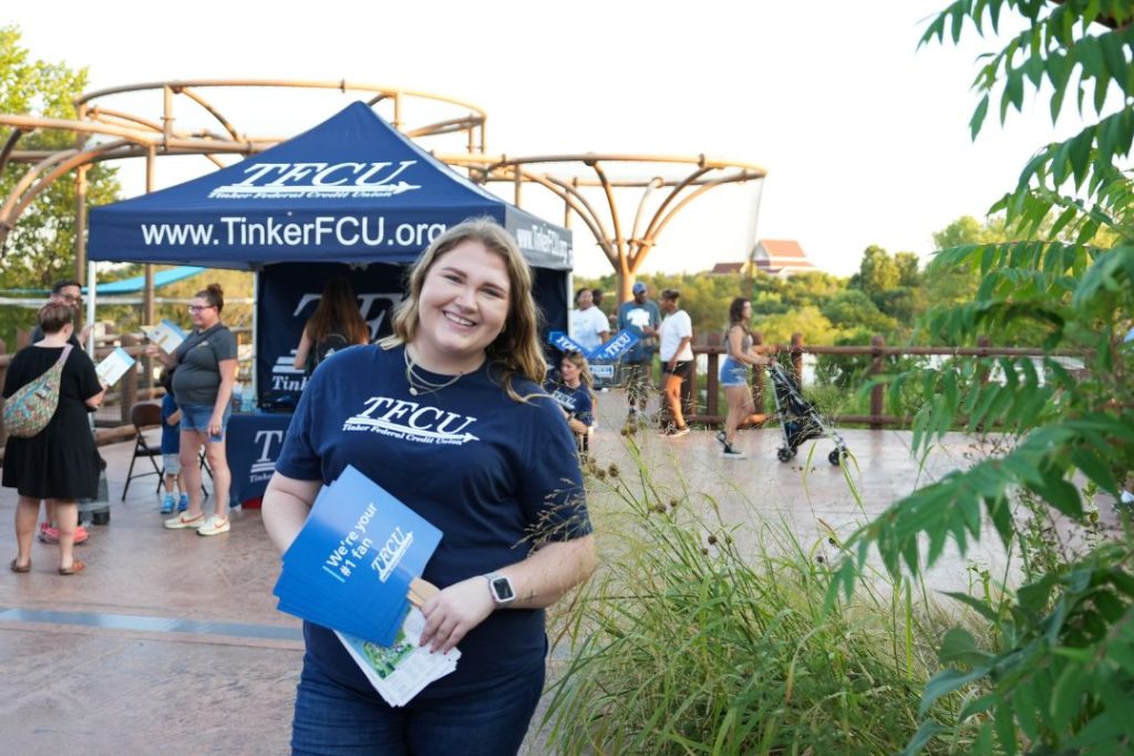 A TFCU employee smiles while holding TFCU hand fans at the zoo
