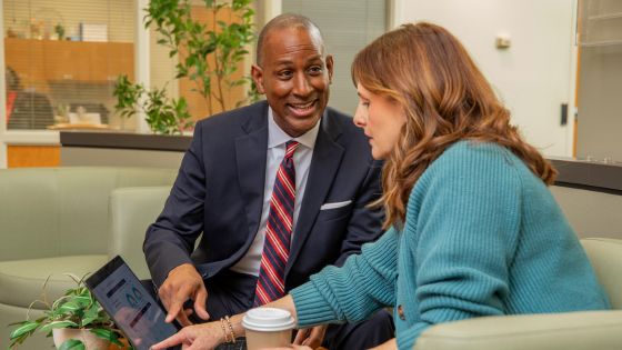 A man in a suite shows a woman something on a laptop