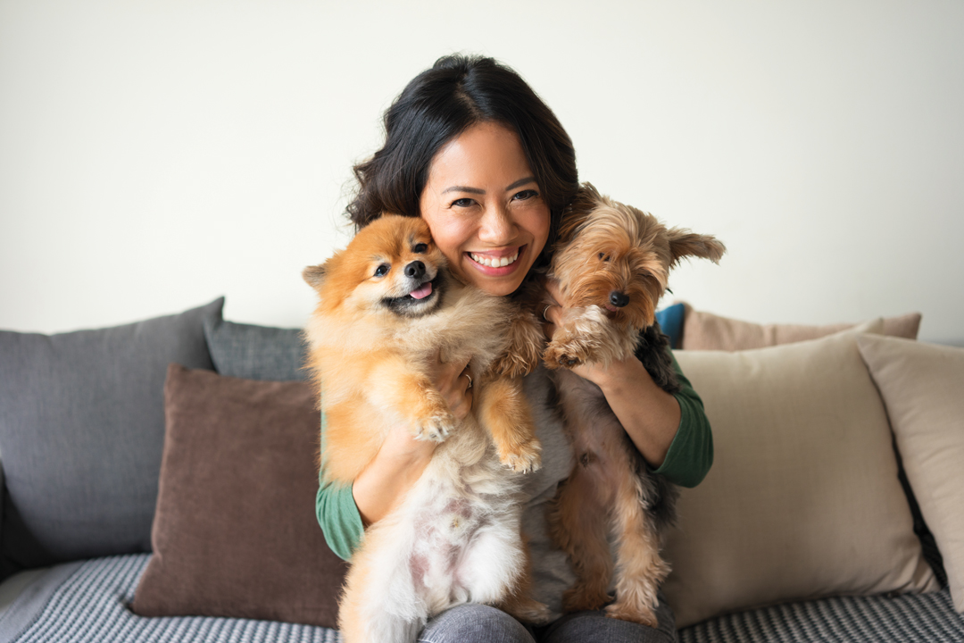 Smiling woman sitting on couch, cuddling two small dogs