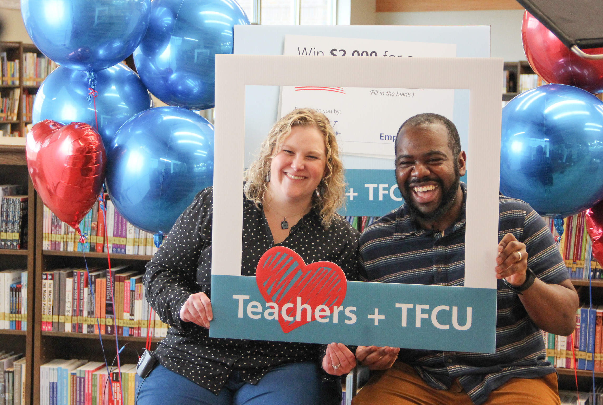 Two people holding up a sign that says Teachers + TFCU