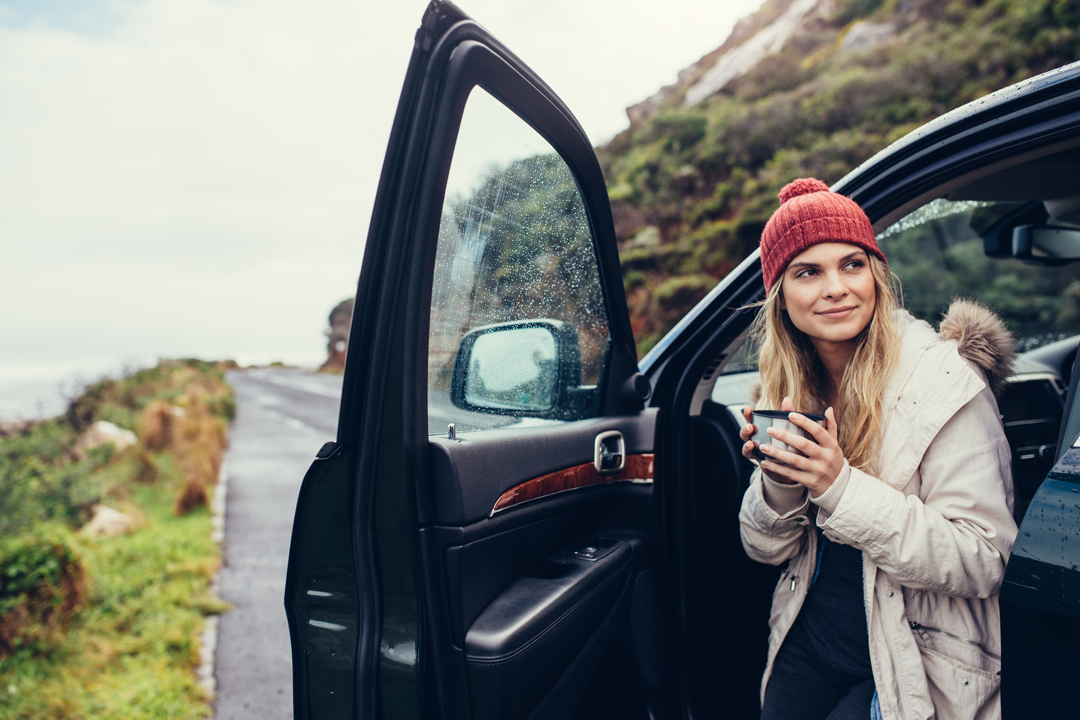 Young woman in red knit hat drinking coffee on a road trip