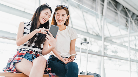 Young girls looking at phone and smiling while waiting in an airport terminal.
