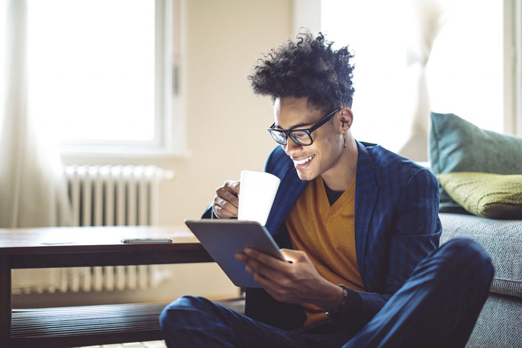 Young man holding mug and reading from tablet.