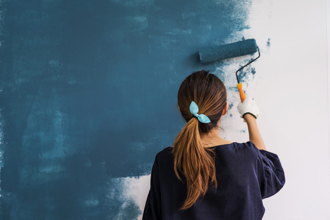 Young woman with hair in pony tail painting a wall blue.