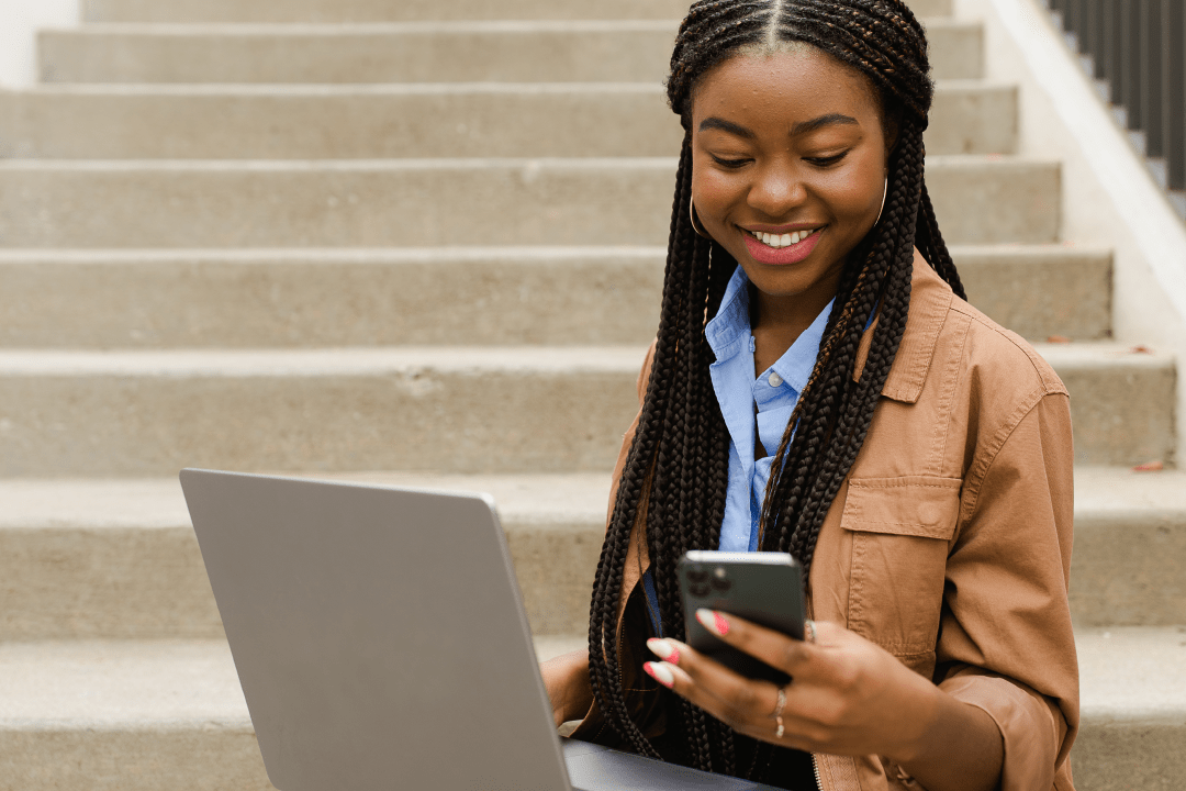 Young woman sitting on steps with her laptop and on a mobile device