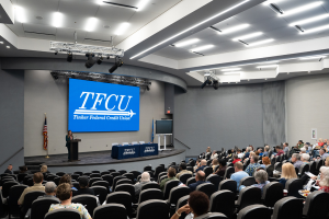 Conference room of people with a speaker on the stand talking about fraud.