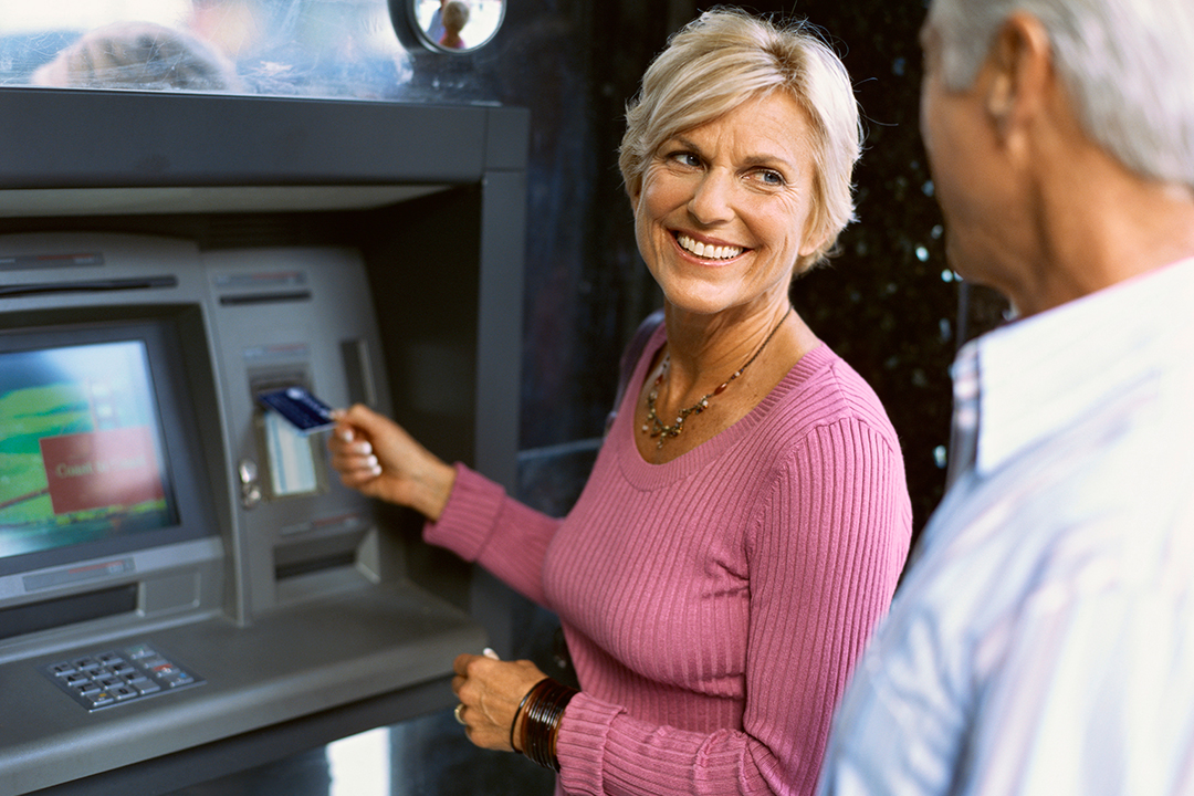 Older woman using ATM while smiling at husband