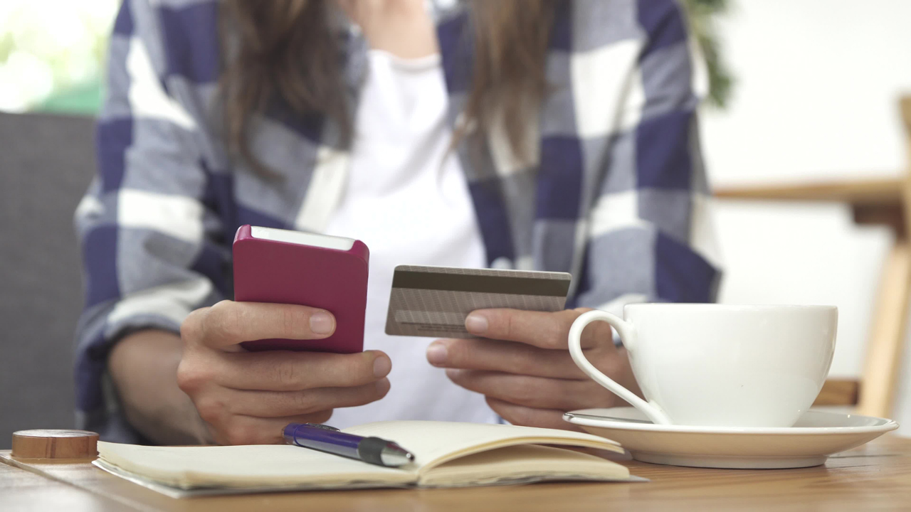 Young woman in blue checked shirt on her smartphone and using a credit card